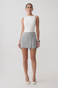 Woman wearing a white sleeveless top and grey wrap mini skirt.
