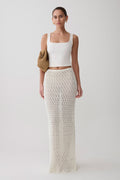 Woman wearing a white sleeveless top and white knit crochet skirt.