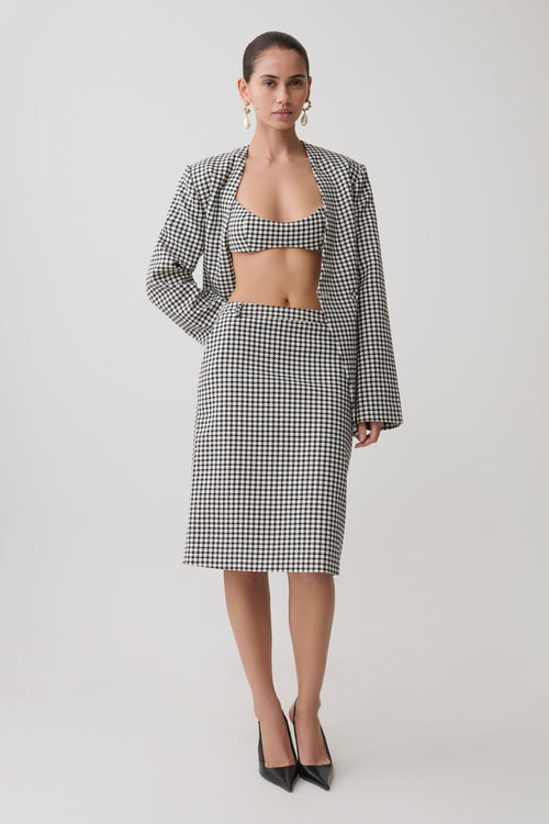 Woman wearing a black and white tweed checkered bralette with matching blazer and midi skirt.