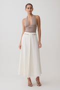 Woman wearing a brown halter top and peral button white midi skirt.