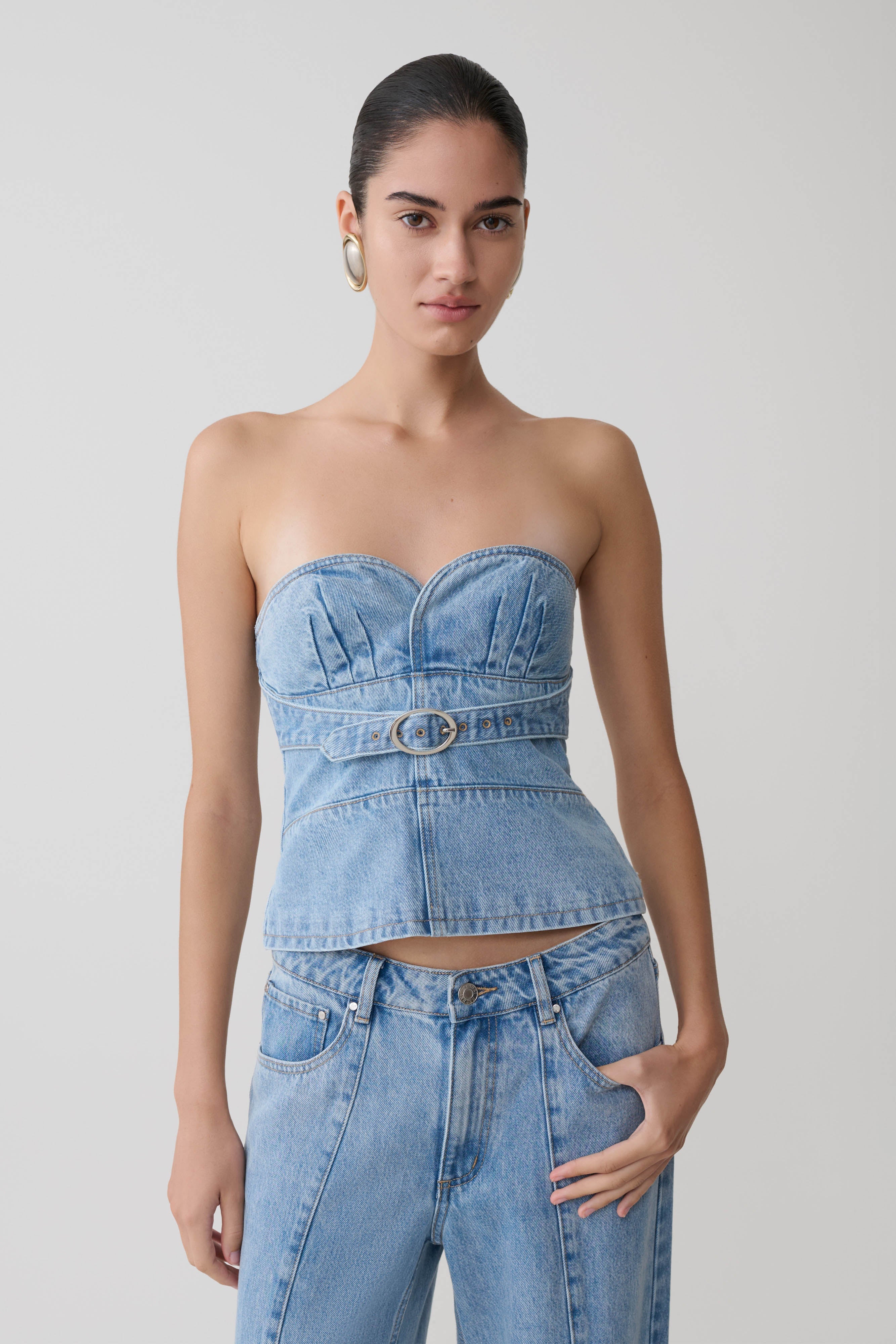 Woman wearing a denim strapless top and high-waisted jeans against a plain background.