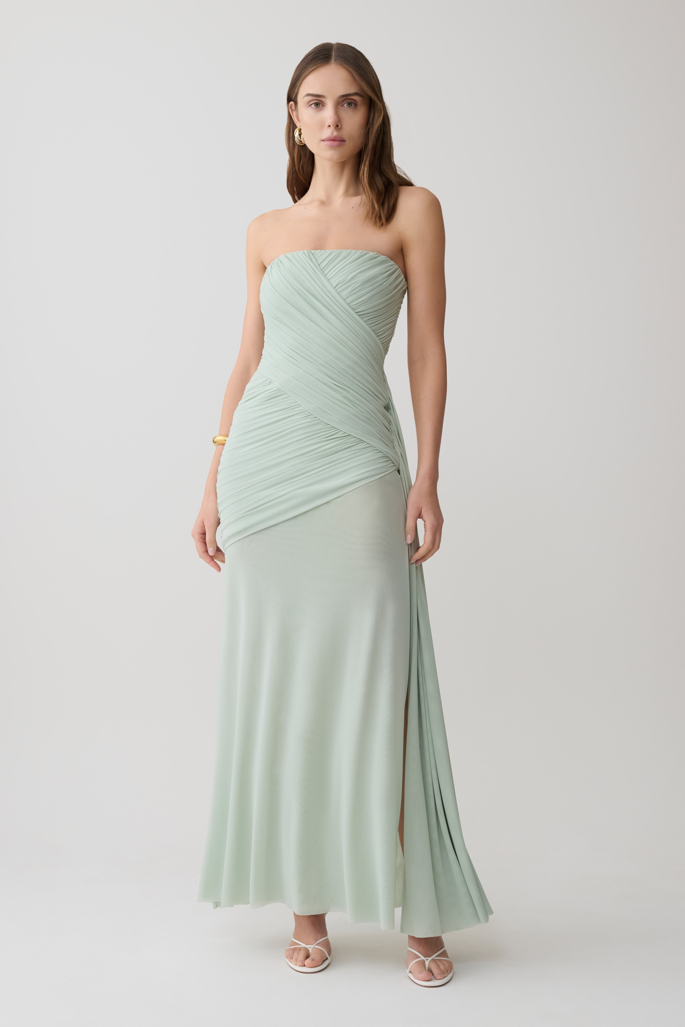 Woman wearing a light green strapless ruched mesh maxi dress.